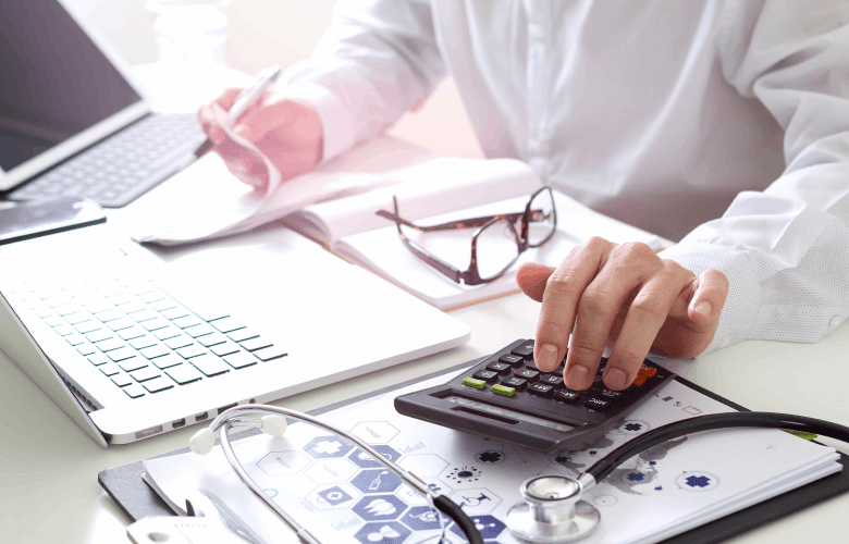 Een man in een wit hemd berekent ziekenhuiskosten met een rekenmachine en een volle bureau.