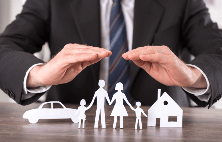 Een man in een kostuum met een das houdt zijn handen boven een papieren gezin met een auto en een huis.